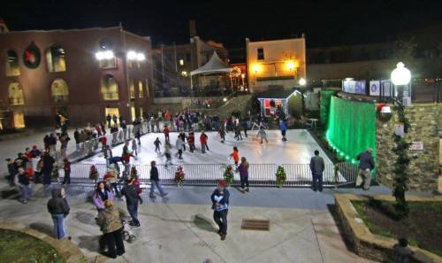 A lively outdoor ice skating rink at night, surrounded by festive lights and a crowd of skaters and onlookers.