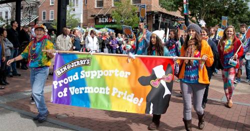 A colorful parade scene with people holding a "Proud Supporter of Vermont Pride" banner, celebrating diversity and inclusion.