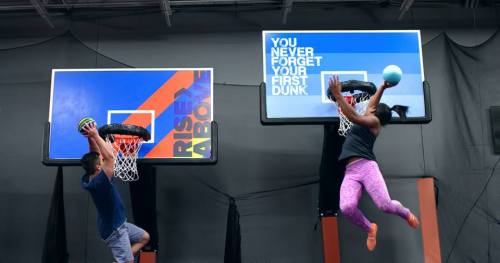 Two people jumping to dunk basketballs on two hoops, with motivational signs in the background.