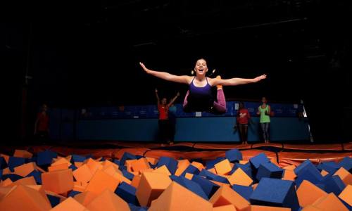 A person joyfully leaps into a foam pit, surrounded by colorful foam blocks, with others in the background.