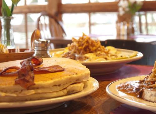 A close-up of a breakfast table featuring pancakes with bacon, a plate of nachos, and a side of syrup.