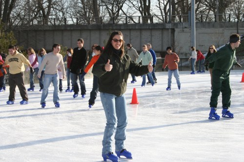 A group of people ice skating on an outdoor rink, with one person giving a thumbs-up in the foreground.