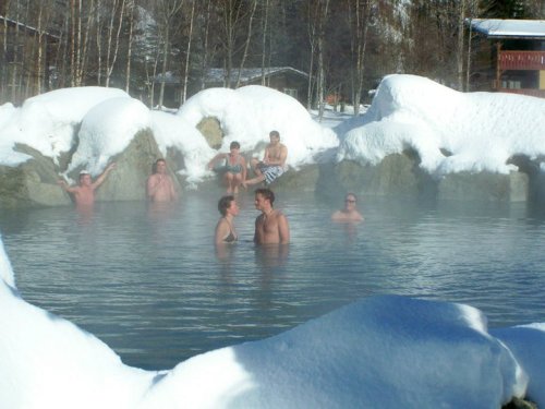 People enjoying a steaming hot spring surrounded by snow-covered rocks and winter scenery.