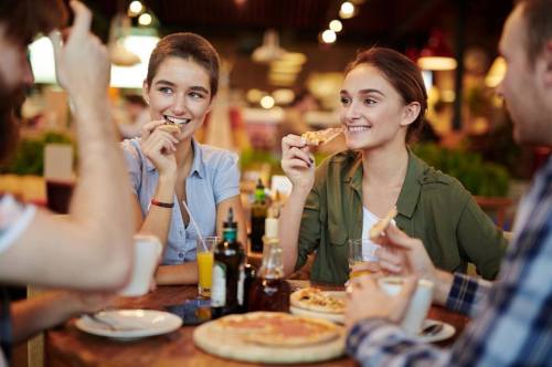 A group of friends enjoying pizza and drinks at a cozy restaurant, smiling and sharing a meal together.