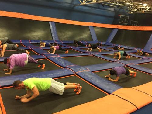 A group of people doing plank exercises on a trampoline court, surrounded by colorful safety pads.