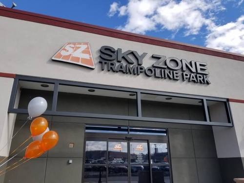 Exterior of Sky Zone Trampoline Park with orange and white balloons at the entrance under a blue sky.
