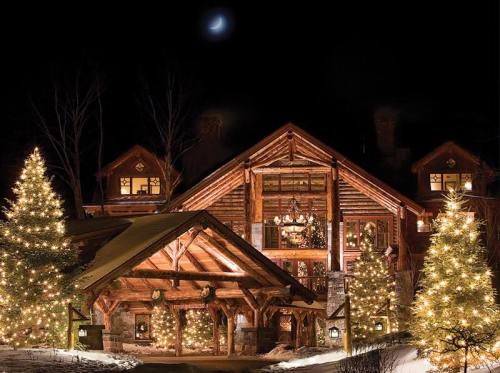 A cozy log cabin decorated with Christmas lights and surrounded by snow-covered trees at night.