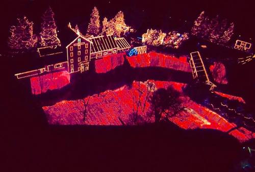 Aerial view of a brightly lit landscape with a building and trees illuminated in colorful lights at night.