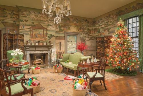 A cozy holiday living room with a decorated Christmas tree, festive decor, and a fireplace surrounded by vintage furniture.