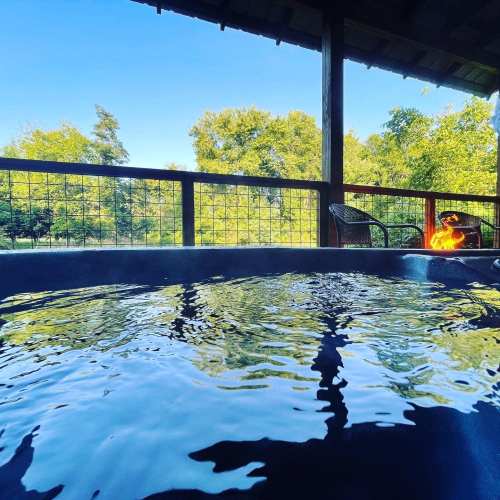 A serene view of a hot tub on a deck, surrounded by trees and a clear blue sky.