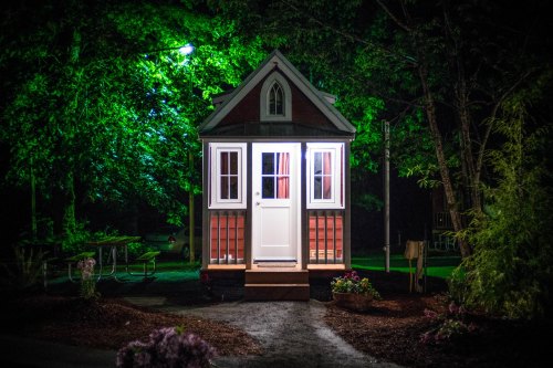 A small, illuminated house surrounded by trees at night, with a welcoming front door and soft light glowing from inside.