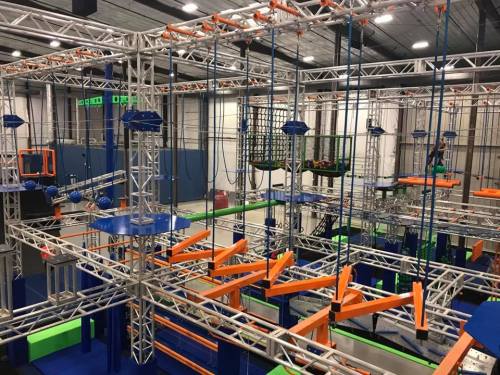 An indoor adventure course featuring climbing structures, ropes, and obstacles in a spacious facility.