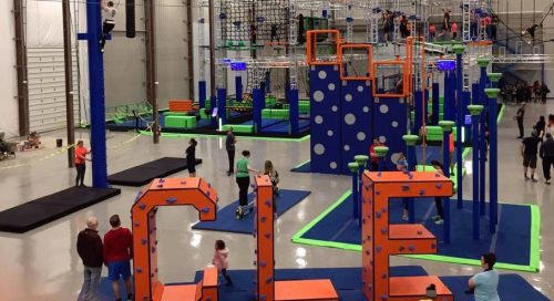 A vibrant indoor obstacle course with climbing structures, nets, and colorful equipment, featuring the letters "CLE" in the foreground.
