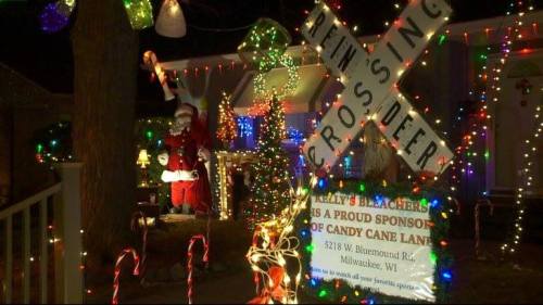 A festive house decorated with colorful lights, featuring a Santa figure and a sign for a candy cane lane event.