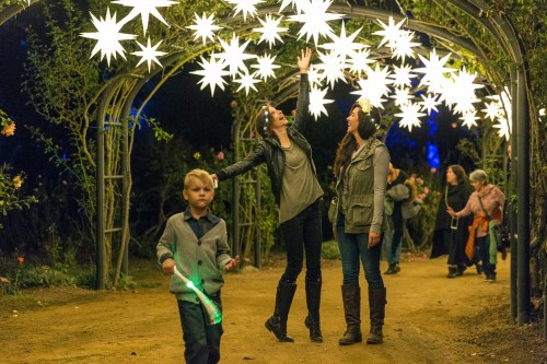 Two women admire glowing star decorations while a boy plays with a light stick in a festive outdoor setting.