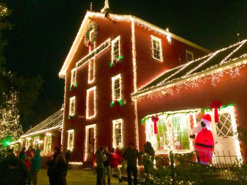 A festive red building adorned with Christmas lights and decorations, with people gathered outside enjoying the holiday spirit.