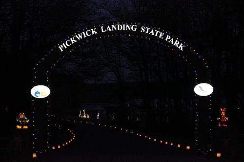 Archway entrance to Pickwick Landing State Park, illuminated with festive lights, leading down a candlelit path at night.