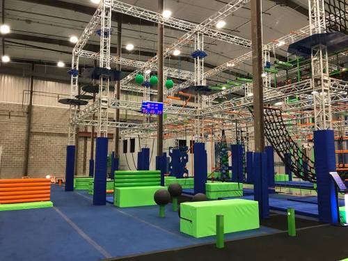 Indoor obstacle course featuring colorful climbing structures, foam blocks, and various challenges in a spacious facility.
