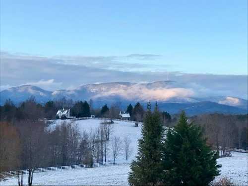 A snowy landscape with a white house, trees, and mountains in the background under a clear blue sky.