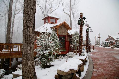 A snowy scene featuring a cozy cabin surrounded by trees and festive decorations along a brick pathway.