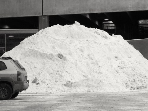 A large mound of snow beside a parked car in a parking garage.
