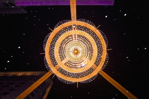 A large, ornate chandelier hangs from above, surrounded by falling snow against a dark night sky.
