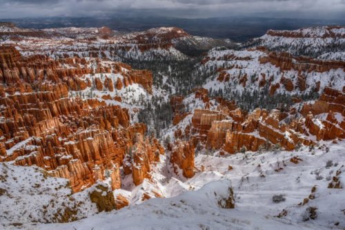A snowy landscape of red rock formations and canyons under a cloudy sky, showcasing the beauty of nature.