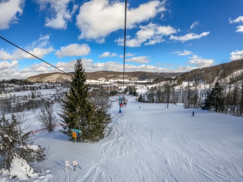 A scenic view from a ski lift, overlooking snowy slopes and a valley under a blue sky with fluffy clouds.