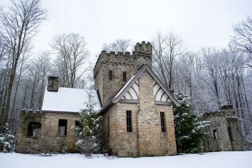 A snow-covered stone castle surrounded by bare trees in a winter landscape.