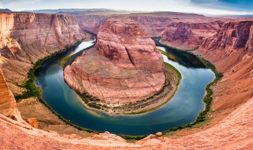 A panoramic view of Horseshoe Bend, featuring a winding river surrounded by towering red rock formations.