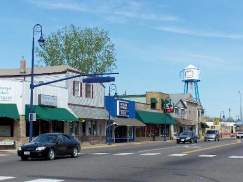 A small town street with shops, green awnings, and a water tower in the background under a clear blue sky.