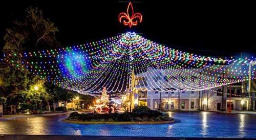 Colorful holiday lights drape over a festive plaza at night, creating a vibrant and cheerful atmosphere.