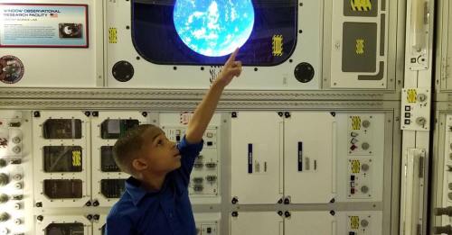 A child points at a glowing globe display inside a space-themed exhibit.