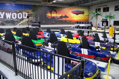 A row of colorful go-karts lined up in an indoor racing facility with a tropical-themed mural in the background.