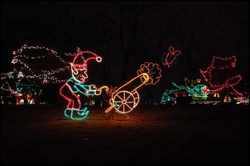 Colorful holiday lights depict an elf with a cannon, surrounded by festive decorations in a nighttime setting.