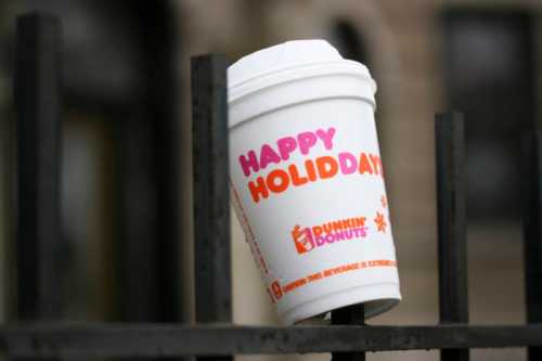 A Dunkin' Donuts cup with "Happy Holidaze" printed on it, resting on a black metal railing.