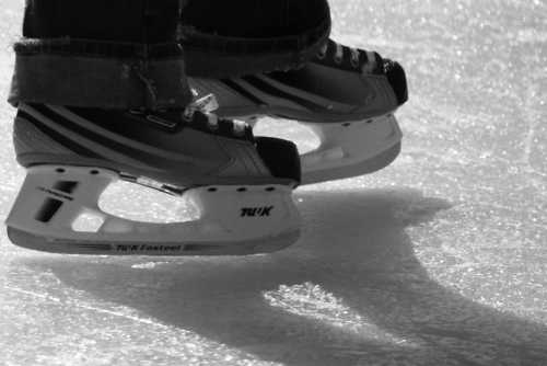 Close-up of ice skates gliding on ice, casting a shadow in black and white.