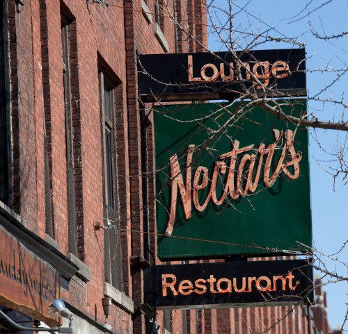 Sign for Neatar's Restaurant and Lounge, featuring a green background with orange lettering, against a brick building.