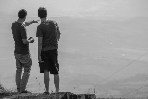 Two men stand on a hillside, pointing and looking out over a misty landscape.