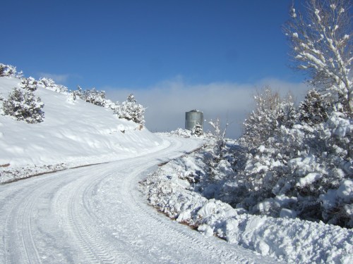 A snowy landscape with a winding road leading to a silvery water tower under a clear blue sky.