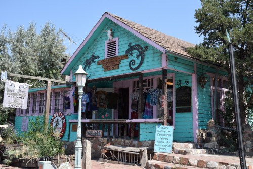 A colorful turquoise shop with a porch, displaying various items and surrounded by greenery.