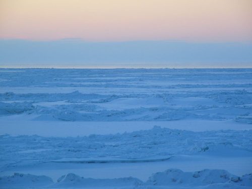 A serene icy landscape with snow-covered terrain under a soft pastel sky at dawn.