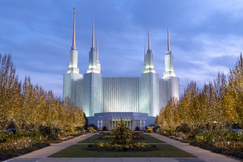 A grand building with tall spires, surrounded by trees adorned with festive lights, under a twilight sky.