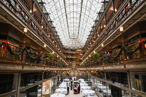 Elegant indoor atrium with glass ceiling, decorated for the holidays, featuring dining tables and festive greenery.