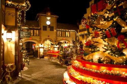 A festive street scene adorned with Christmas lights, decorations, and a large tree surrounded by shops.