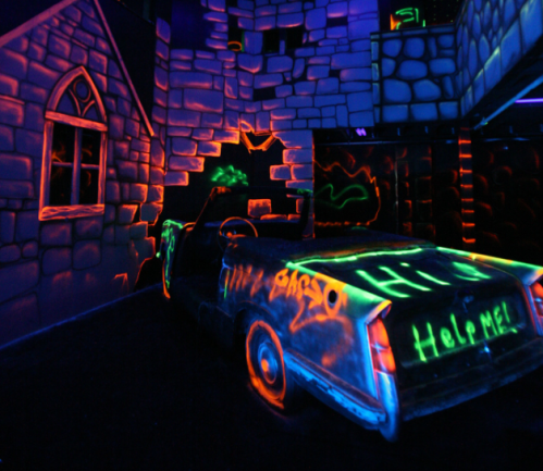 A glowing, graffiti-covered car inside a dark, neon-lit room resembling a haunted house.