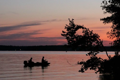 Silhouetted fishermen in a boat on a calm lake at sunset, with vibrant colors reflecting on the water.