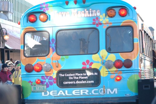 Colorful bus with floral designs and a sign promoting careers at Dealer.com. People are visible in the background.
