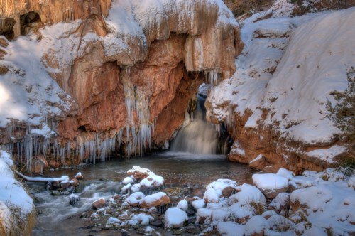 A serene winter scene featuring a waterfall cascading through a rocky cave, surrounded by snow and icicles.