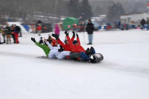 A group of people in colorful winter gear sledding down a snowy hill, all raising their arms in excitement.